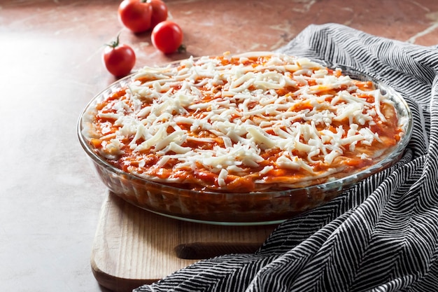 Domowa lasagne gotowa do pieczenia w okrągłym szklanym naczyniu do pieczenia na desce