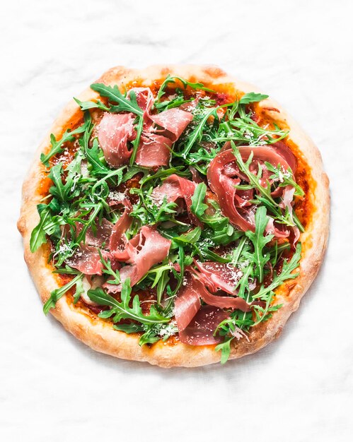 Domowa pizza z prosciutto w sosie pomidorowym i rukolą na jasnym tle widok z góry