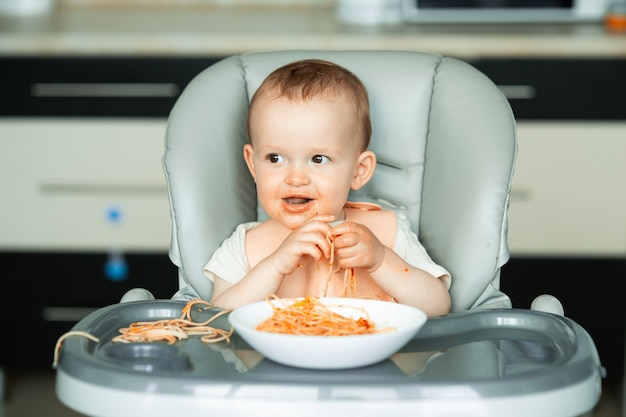 Domowa scena z małym chłopcem je spaghetti roczny chłopiec je makaron w domu w ...