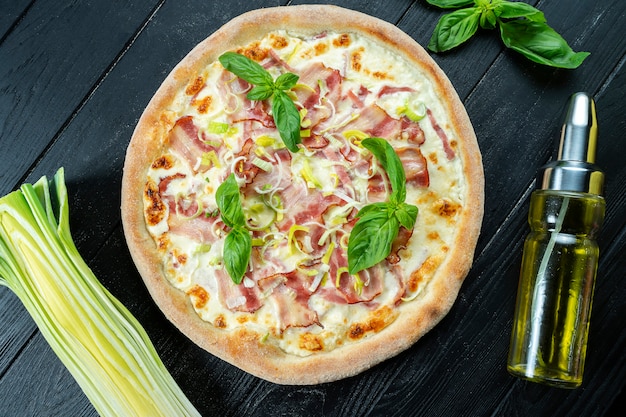 Domowa świeża pizza Carbonara z białym sosem bekonowym na czarnym drewnianym z miejsca kopiowania. Zdjęcie jedzenia z góry.