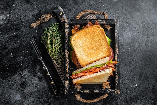 Zdjęcie domowa tostowana kanapka blt z bekonem, pomidorem i sałatą w drewnianej tacy. czarne tło. widok z góry.