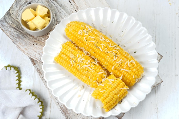 Zdjęcie domowa złota kolba słodkiej kukurydzy z masłem i serem na białym stole