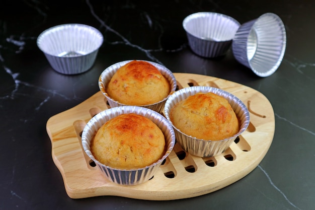 Domowe babeczki bananowe w formie na drewnianej desce do chleba z pustą aluminiową foremką na muffinki na stole w kuchni z czarnego marmuru