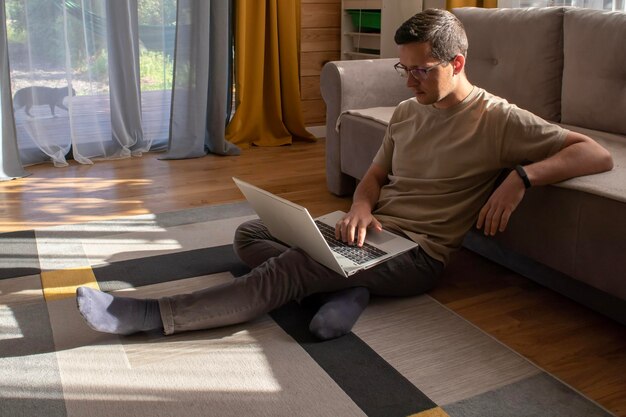 Domowe biuro w słonecznym mieszkaniu na poddaszu Mężczyzna siedzący przy komputerze i pracujący na podłodze