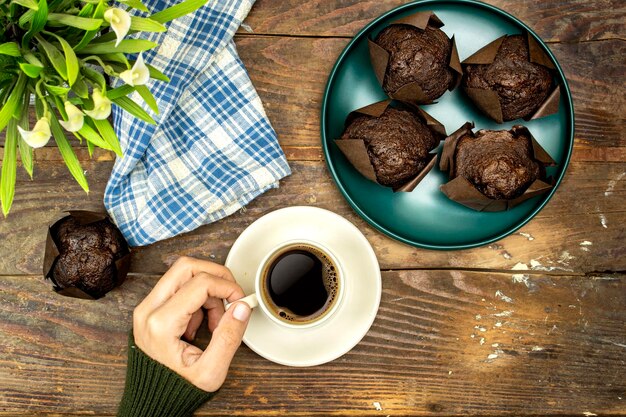 Domowe ciasteczka czekoladowe lub madeleine w zielonym talerzu i kobieta pijąca kawę lilie kwiaty o