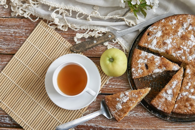 Domowe ciasto z wiśniami i jabłkami biała filiżanka herbaty na tle ciemnej rustykalnej drewnianej desce. Jedzenie w stylu rustykalnym