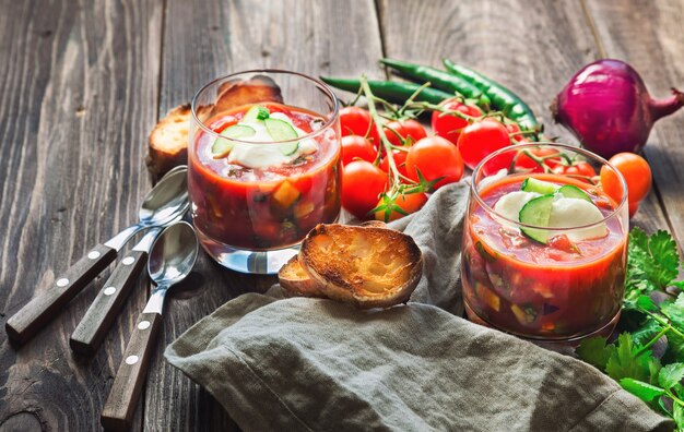 Domowe gazpacho zupa pomidorowa w szklankach z opiekanym chlebem na rustykalnym drewnianym tle