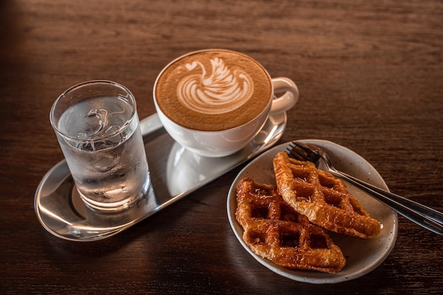 Domowe gofry belgijskie z miodem i gorącą kawą latte z pianką mleczną latte art w kształcie łabędzia w kubku na drewnianym biurku na widoku z góry jako śniadanie w kawiarni w kawiarni podczas pracy biznesowej