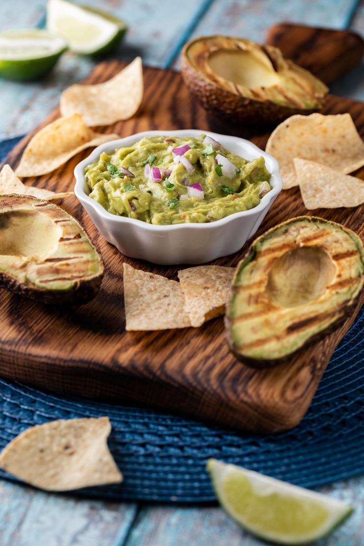 Zdjęcie domowe guacamole otoczone grillowanymi awokado i chipsami tortilla