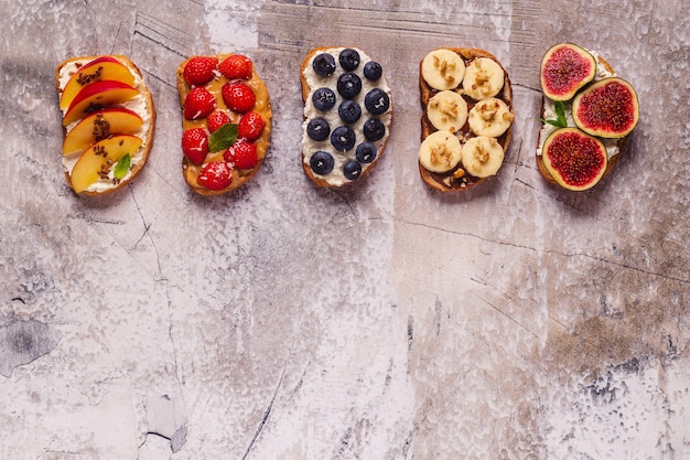 Zdjęcie domowe letnie tosty z twarogiem, masłem orzechowym oraz owocami i jagodami, widok z góry.