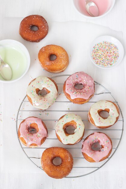 Domowe pączki ozdobione kolorowym lukrem i kolorowym cukrem na jasnym tle.