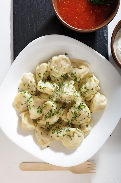 Domowe pierogi w kuchni bez ozdób. gotowe pierogi na białym talerzu, podawane z kwaśną śmietaną i adjika