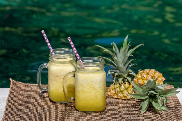 Zdjęcie domowe smoothie z mango i ananasa z mlekiem kokosowym w dwóch szklanych kubkach w pobliżu basenu wyspa bali indonezja orzeźwiający napój z owoców tropikalnych