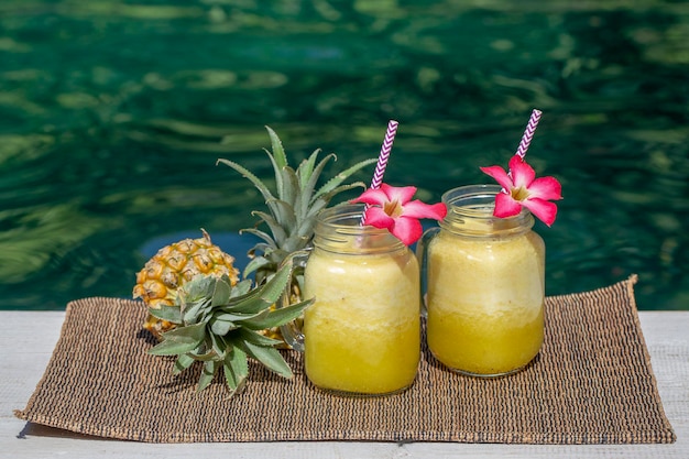 Zdjęcie domowe smoothie z mango i ananasa z mlekiem kokosowym w dwóch szklanych kubkach w pobliżu basenu wyspa bali indonezja orzeźwiający napój z owoców tropikalnych