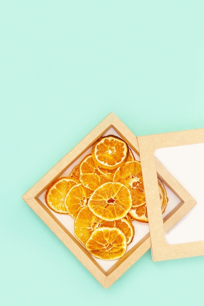 Zdjęcie domowe suszone chipsy owocowe mandarynki na niebiesko. sucha mandarynka w papierowym opakowaniu. dietetyczne jedzenie