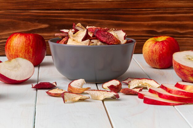 Domowe suszone jabłka ze świeżymi jabłkami na lekkim drewnianym stole.
