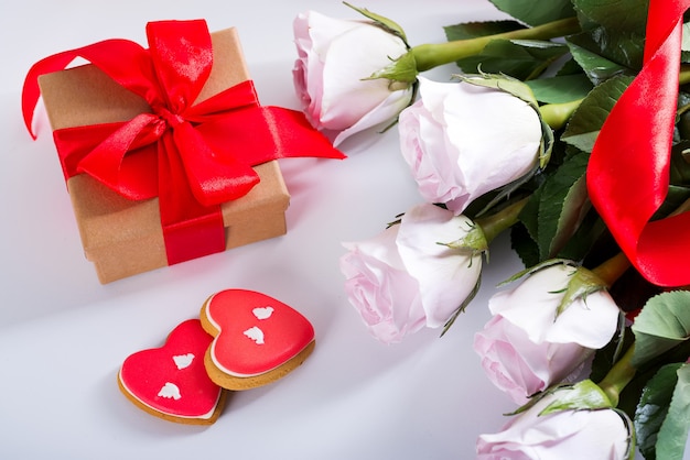 Zdjęcie domowe walentynki serca ciasteczka, różowe róże i czerwone pudełko na białym stole