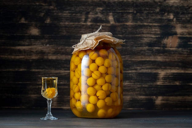 Domowej roboty nalewka z żółtej śliwki wiśniowej w szklanym słoju i kieliszku do wina na drewnianym tle Ukraina z bliska
