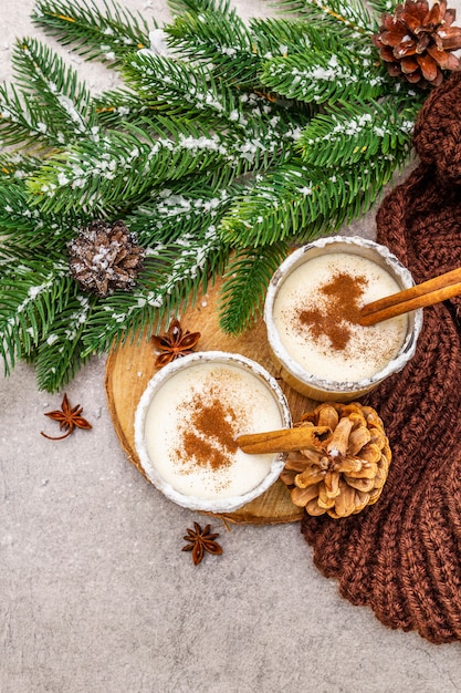 Domowy ajerkoniak z cynamonem w szkle. Typowy świąteczny deser. Zimozielony brunch z jodły, szyszki, przytulna kratka, sztuczny śnieg.