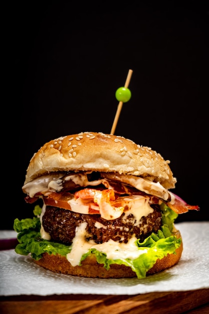 Domowy burger wołowy z pomidorami sałaty i serem na drewnianej desce z czarnym tłem Widok normalny Skopiuj tekst Koncepcja Fastfood