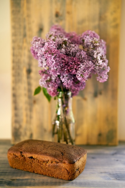 Domowy chleb żytni bez drożdży leży na drewnianym stole obok bukietu bzu