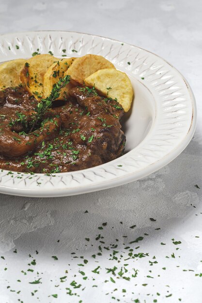 Domowy gulasz z mięsa osso buco z aromatycznym sosem ziołowym, czerwonym winem i frytkami