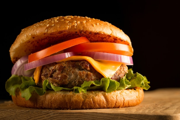 Domowy hamburger z wołowiną, cebulą, pomidorem, sałatą i serem. Świeży burger z bliska na drewnianym stole rustykalnym z frytkami, piwem i frytkami. Cheeseburger.