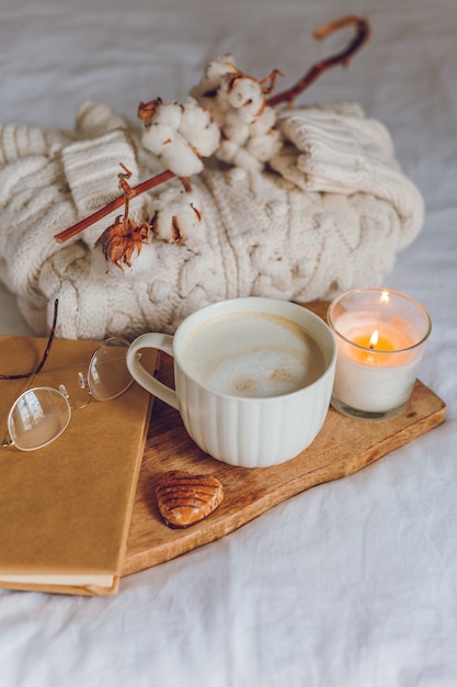 Domowy przytulny wystrój. Kubek cappuccino, ciasteczka, świeca na łóżku. Zimowy poranek. Jesień.