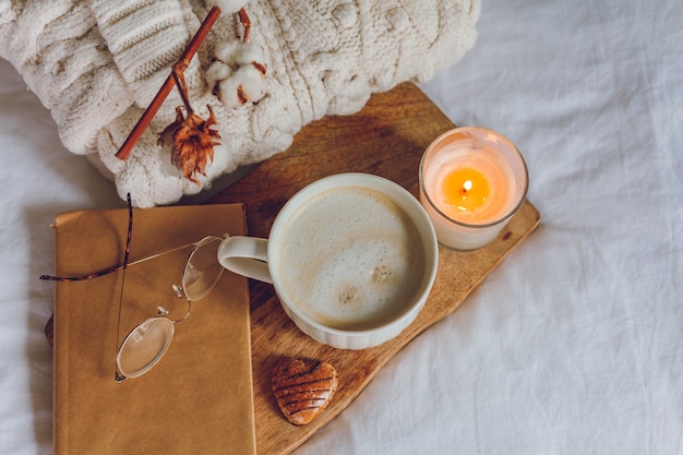 Domowy przytulny wystrój. Kubek cappuccino, ciasteczka, świeca na łóżku. Zimowy poranek. Jesień.