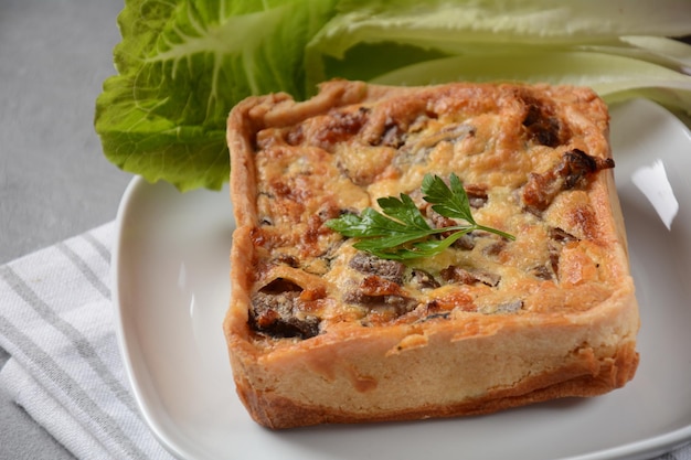 Domowy quiche lub ciasto z brokułami, przyprawami, pieczarkami i serem na szarym tle.