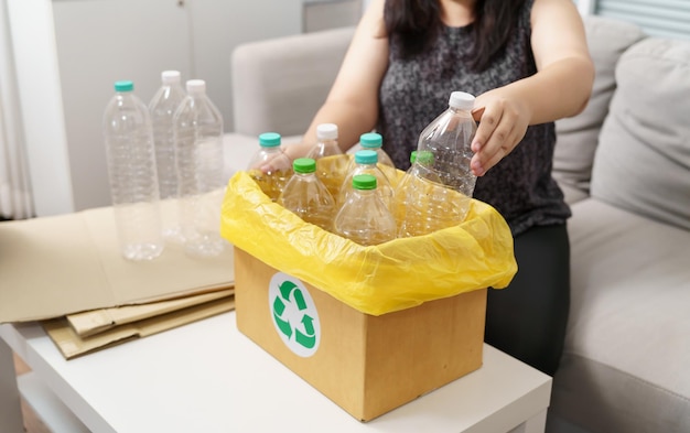 Domowy recykling eco zielony zerowy pojęcie Kobieta rzuca pustą plastikową butelkę w koszu z żółtymi workami na śmieci w domu