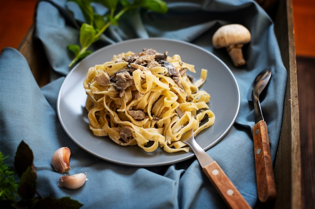 Domowy włoski makaron fettuccine z pieczarkami i sosem śmietanowym podany na szarym talerzu z bazylią (Fettuccine al Funghi Porcini). Tradycyjna kuchnia włoska. Ciemny nieociosany drewniany tło, zakończenie