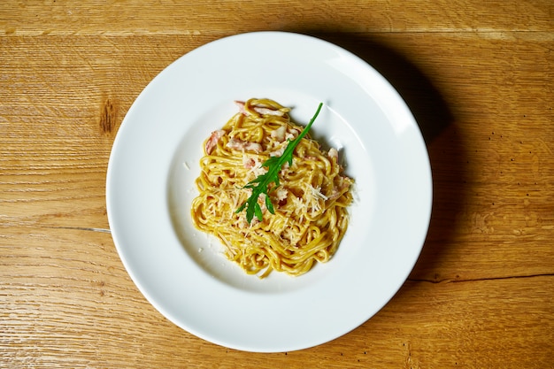 Domowy włoski makaron w kremowym sosie, boczku i parmezanem w białym talerzu. Kuchnia włoska .. Stół do zdjęć ze smacznym jedzeniem