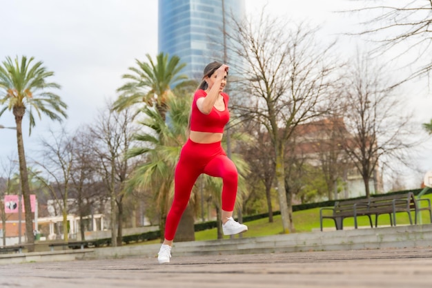 Dopasowana kobieta w czerwonych ubraniach robi ćwiczenia joggingowe w miejskim sporcie fitness