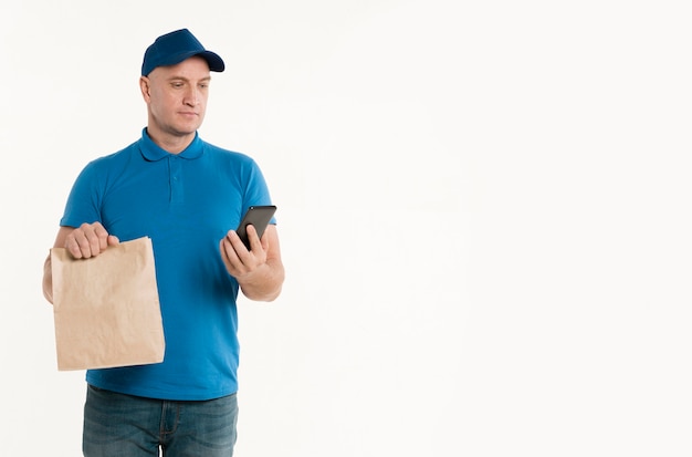 Zdjęcie doręczeniowy mężczyzna patrzeje smarthpone z papierową torbą