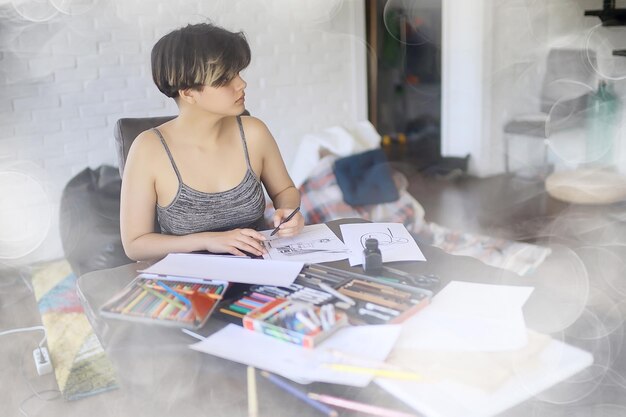 dorosła dziewczyna rysuje ołówkiem na papierze / portret pięknej młodej studentki, edukacja w szkole artystycznej, koncepcja edukacji artystycznej