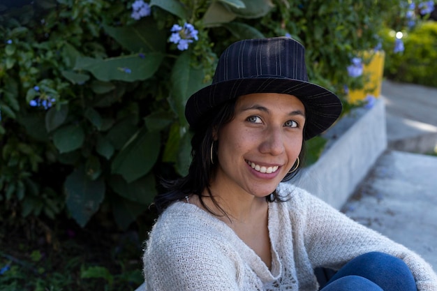 Dorosła latynoska kobieta siedzi w parku, patrząc w kamerę z uśmiechem i pozytywnym nastawieniem