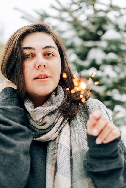 Zdjęcie dorosła młoda kobieta z zimnymi ogniami na zimowym sosnowym lesie