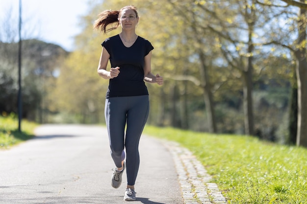 Dorosła uśmiechnięta kobieta fitness jogging na torze w parku
