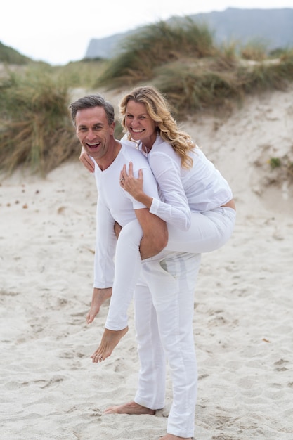 Dorośleć mężczyzna daje piggyback przejażdżce kobieta na plaży