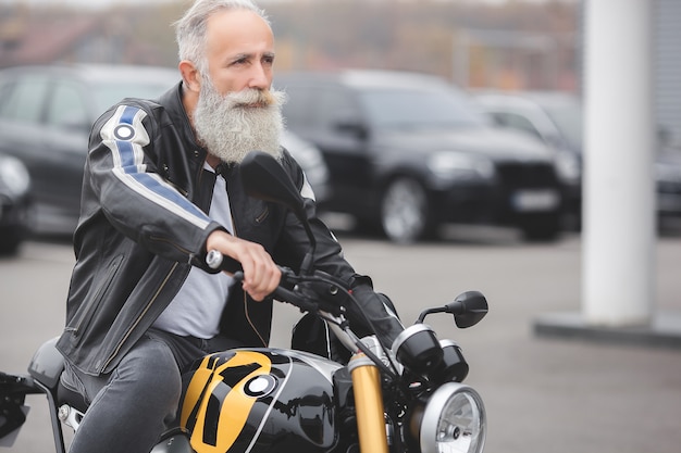 Dorośleć mężczyzna jedzie motocykl. Stary mężczyzna na motocyklu. Brodaty mężczyzna na zewnątrz jazdy.