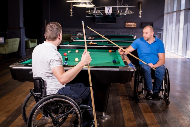 Dorośli mężczyźni niepełnosprawni na wózku inwalidzkim grają w bilard w klubie