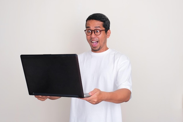 Dorosły Azjat wykazuje wyraz twarzy, gdy patrzy na laptop