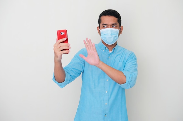 Dorosły Azjata Noszący Maskę Medyczną Pokazującą Znak Stopu, Gdy Patrzy Na Ekran Swojego Telefonu Komórkowego