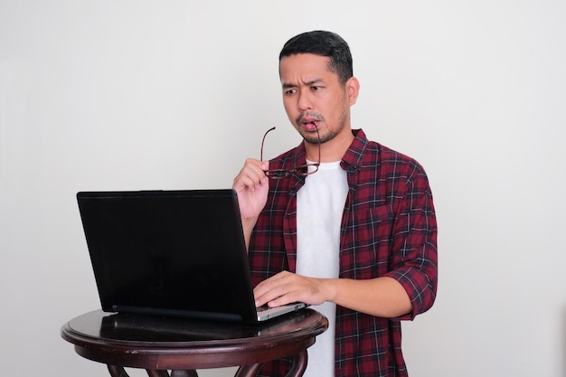 Dorosły azjatycki mężczyzna pracujący przy użyciu swojego laptopa z poważnym wyrazem twarzy