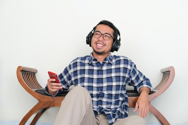Dorosły azjatycki mężczyzna relaksuje się podczas słuchania muzyki ze szczęśliwym wyrazem twarzy