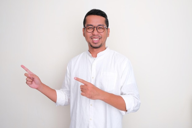 Dorosły azjatycki mężczyzna uśmiecha się do kamery i wskazuje ręką na prawą stronę