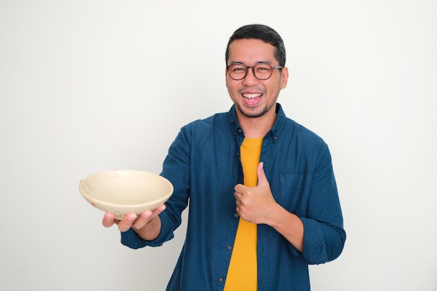 Dorosły azjatycki mężczyzna uśmiecha się i podnosi kciuk, pokazując pustą miskę obiadową