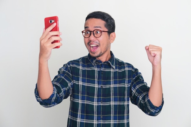 Dorosły azjatycki mężczyzna zacisnął pięść, pokazując szczęście, patrząc na swój telefon