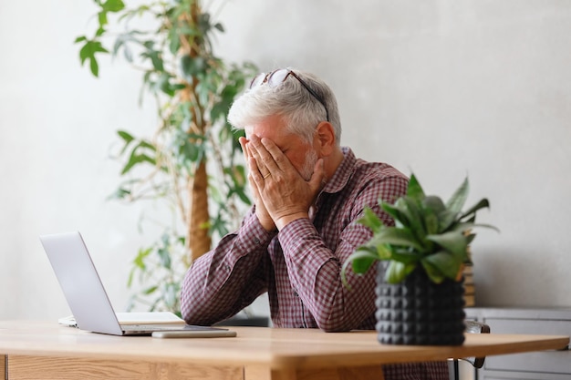 Dorosły człowiek biznesu z siwymi włosami pracuje na laptopie w swoim biurze, w finansach kariery i marketingu